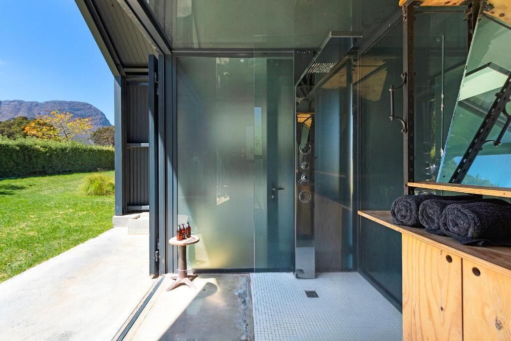A modern building with a glass door leading to a shower area, a small table with bottles, and a wooden cabinet with towels.