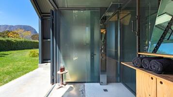 A modern building with a glass door leading to a shower area, a small table with bottles, and a wooden cabinet with towels.