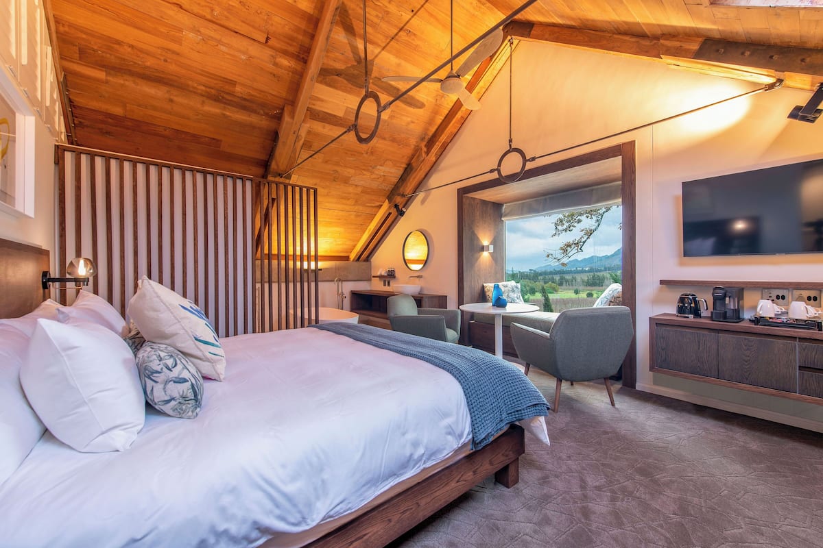 A bedroom with a large bed, a desk, a chair, and a view of the outdoors.