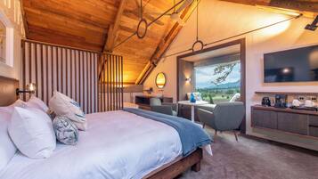 A bedroom with a large bed, a desk, a chair, and a view of the outdoors.
