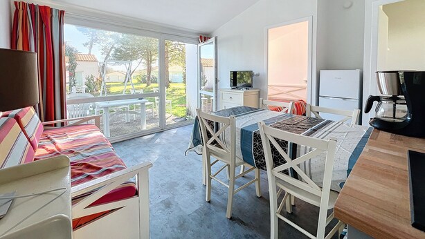 A room with a dining table, chairs, a TV, and a coffee machine. - Maison Dans Résidence Avec Piscine (Dolus-d'Oléron)