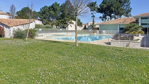 A swimming pool surrounded by a fenced area, with a grassy lawn and trees in the background. - Maison Dans Résidence Avec Piscine (Dolus-d'Oléron)