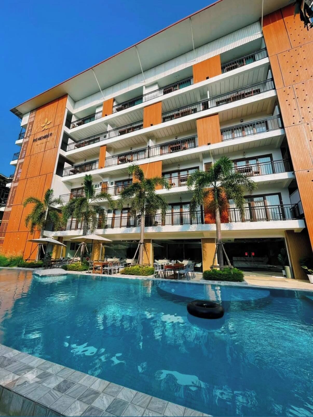 Un hotel de varios pisos con piscina, zona de estar al aire libre y palmeras.