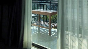 Una habitación con un ventanal grande, un balcón con mesa y vistas a un paisaje montañoso.