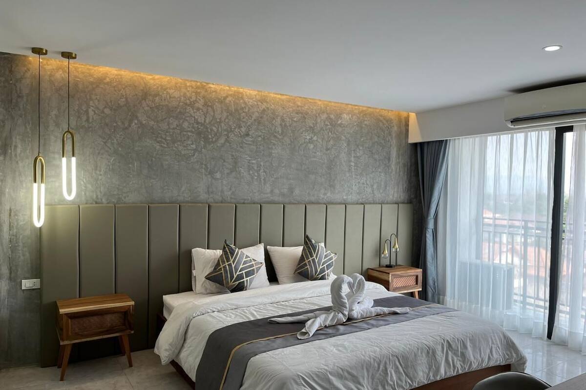 Ein modernes Hotelzimmer mit einem großen Bett, einem Nachttisch aus Holz, einer Nachttischlampe und Blick ins Freie durch große Fenster.