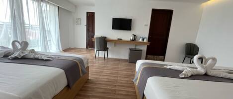 A hotel room with two beds, a desk, a TV, and a view of the outside.