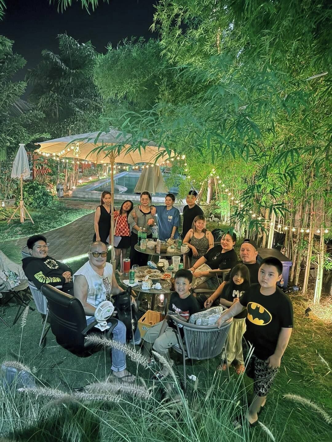 A group of people seated at an outdoor table with a view of a garden and a building in the background.