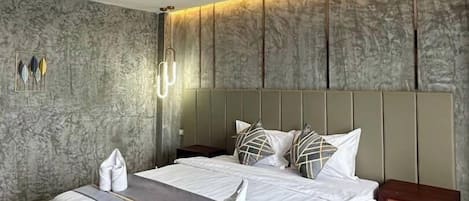 A spacious bedroom with a large bed, a headboard with integrated lighting, a bedside table, and a wall-mounted light fixture.
