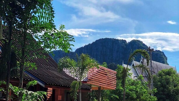 Vista junto a la piscina con una persona relajándose, rodeada de exuberante vegetación y arquitectura tradicional.
