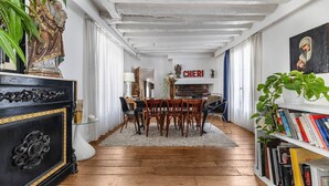 Uma área de refeições com mesa e cadeiras de madeira, um tapete branco e uma estante com livros.