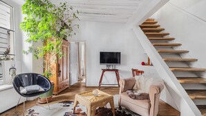 Uma sala de estar com escada, televisão, planta, cadeira e sofá.