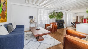 Sala de estar com sofá azul, mesa de centro de madeira e uma planta grande.