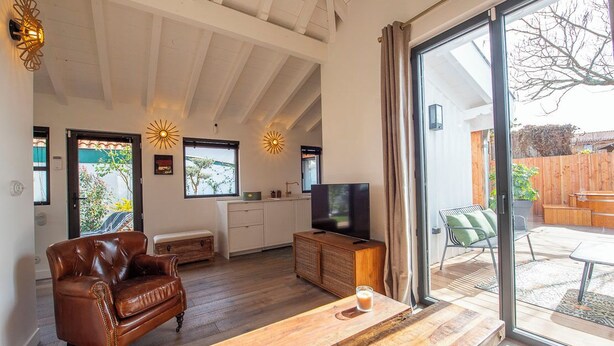 Een ruime woonkamer met een leren bank, een houten salontafel en een televisie. Er zijn grote ramen en een schuifpui die leidt naar een terras.