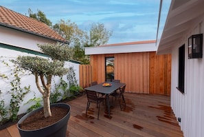 Eine Terrasse mit einem Holztisch und -stühlen, umgeben von einer weißen Mauer und einem Holzzaun.