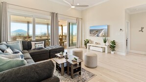 Una sala moderna con un sofá seccional, una mesa de centro y una zona de comedor. Cuenta con un ventanal con vistas a un paisaje urbano y un balcón.