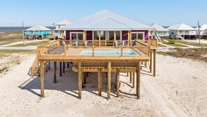 Una casa de playa con terraza de madera y piscina, rodeada de otras casas de playa.