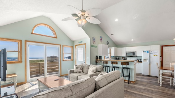 A spacious living area with a large sofa, a dining table, and a kitchen area with a microwave and refrigerator. - Islander: Oceanfront | Hot Tub | Dog-Friendly (Rodanthe)