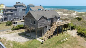 A wooden beach house with a deck and stairs leading to a covered area. - Islander: Oceanfront | Hot Tub | Dog-Friendly (Rodanthe)