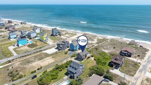 An aerial view of a coastal residential area with houses, a beach, and a marked location for Village Realty. - Islander: Oceanfront | Hot Tub | Dog-Friendly (Rodanthe)
