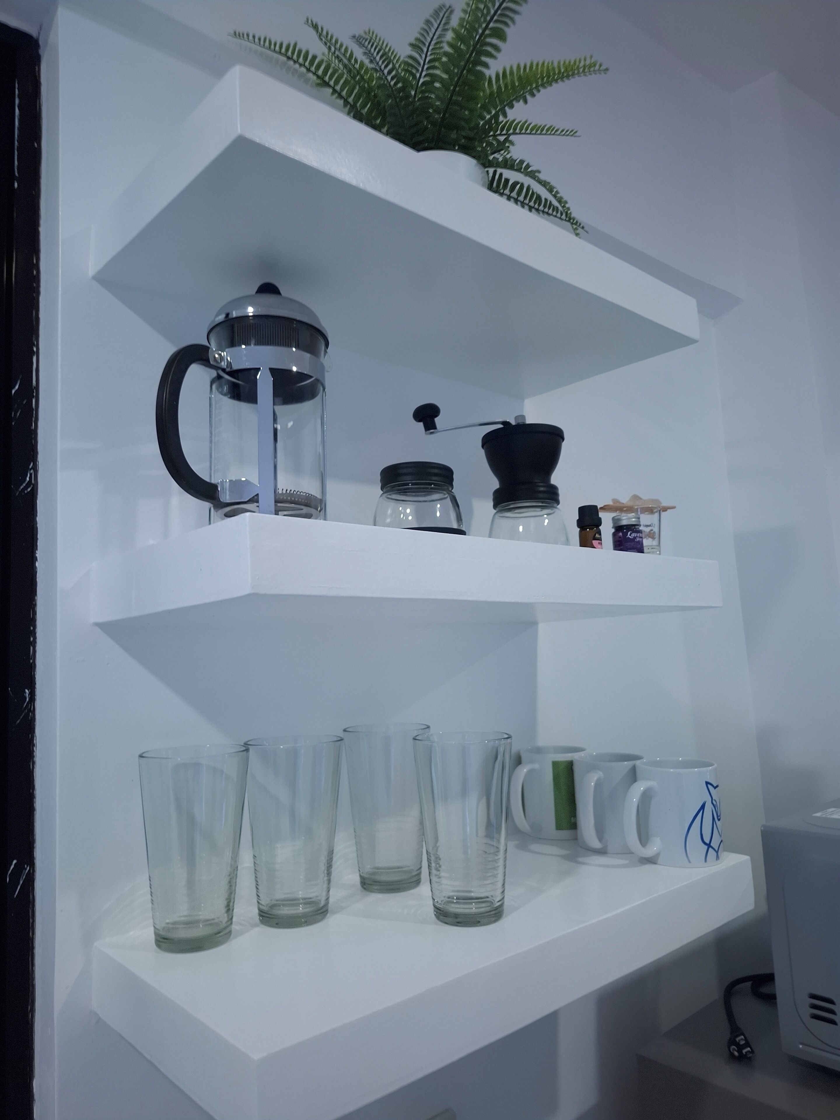 A white shelf with a coffee maker, jars, and glasses.