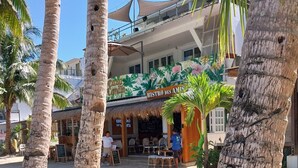 A beachside restaurant with outdoor seating, palm trees, and a building with a tropical mural. - Boracay Luxury Apartments (Boracay Island)
