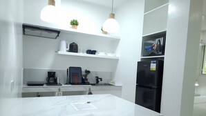 A modern kitchen with a marble countertop, a built-in coffee maker, a black refrigerator, and pendant lighting. - Boracay Luxury Apartments (Boracay Island)
