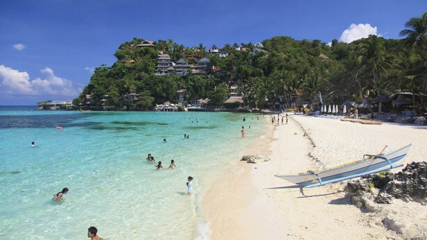 A beach with clear turquoise water, people swimming, and a boat on the shore. - Boracay Luxury Apartments (Boracay Island)