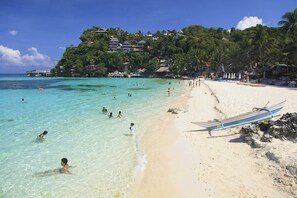 A beach with clear turquoise water, people swimming, and a boat on the shore. - Boracay Luxury Apartments (Boracay Island)