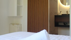 A hotel room with a neatly made bed, a wooden panel wall, a bathroom with a mirror and sink, and a white towel on the bed. - Boracay Luxury Apartments (Boracay Island)