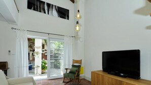 Un salon avec un canapé, un téléviseur posé sur un meuble en bois, un fauteuil et une table avec un set de table.