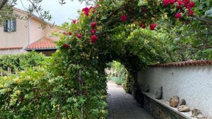 Un sentier de jardin bordé d’un mur de pierres et surmonté d’une arche couverte de plantes grimpantes.