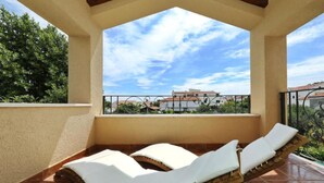 Un balcon avec deux chaises longues, un sol carrelé et une vue sur les bâtiments et les arbres.