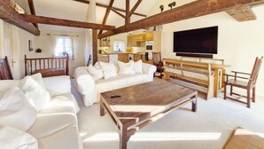 Ein geräumiges Wohnzimmer mit Holzboden, einem großen Flachbildfernseher, einer Couch, einem Couchtisch und einem Essbereich mit Stühlen.