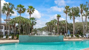 Une piscine avec une fontaine, entourée de palmiers et de chaises longues.