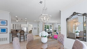 Un coin repas avec une table ronde, des chaises, un lustre et un grand miroir au mur.