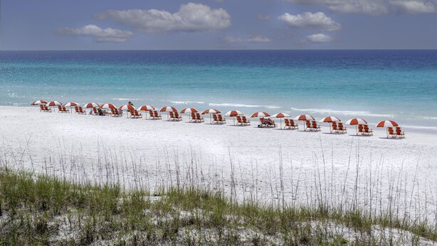 Une plage bordée de rangées de chaises de plage et de parasols rouges et blancs.