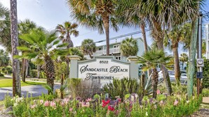 A sign for Sandcastle Beach Townhomes with a landscaped garden in front.