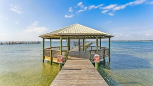 A wooden pier leading to a gazebo with a roof, surrounded by clear water.