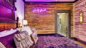 A bedroom with a large bed, a neon sign reading "Lady Bird," and a wooden wall. - 25% Off August!  LBJ Ste, 1 Block To Downtown* (Marble Falls)