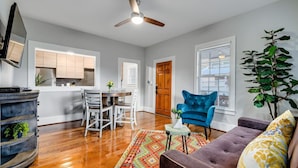 A modern living room with a wooden floor, a blue armchair, a purple sofa, and a dining area with white chairs and a table. - 25% Off Sept,  Inks Suite, 1 Block To Downtown! (Marble Falls)