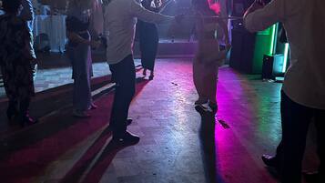 Et dansegulv med dansende mennesker, lyskæder hængt over hovederne og et sceneområde med et bord og stole.