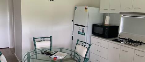 A compact kitchen with white cabinets, a microwave, a refrigerator, and a glass-top dining table with chairs.