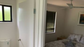 A bedroom with a bed, a window with blinds, a toilet, and a ceiling fan.