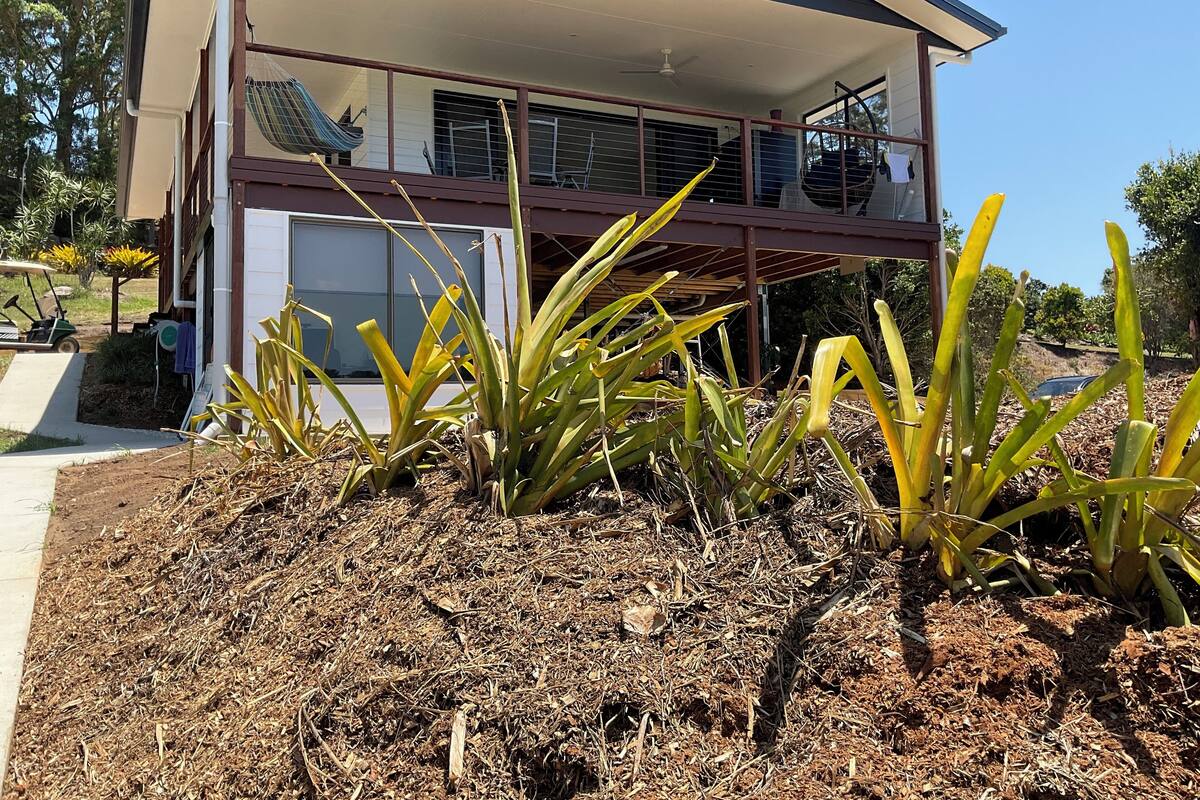 Una casa de dos pisos con un balcón, un porche cubierto y un jardín con plantas.