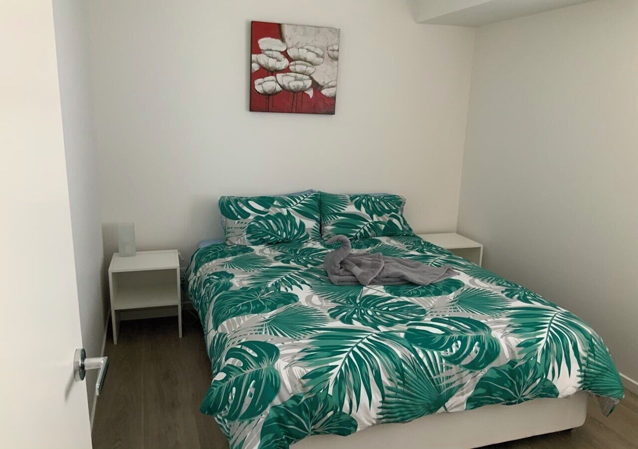 A bedroom with a bed, a nightstand, a wall art piece, and a door.