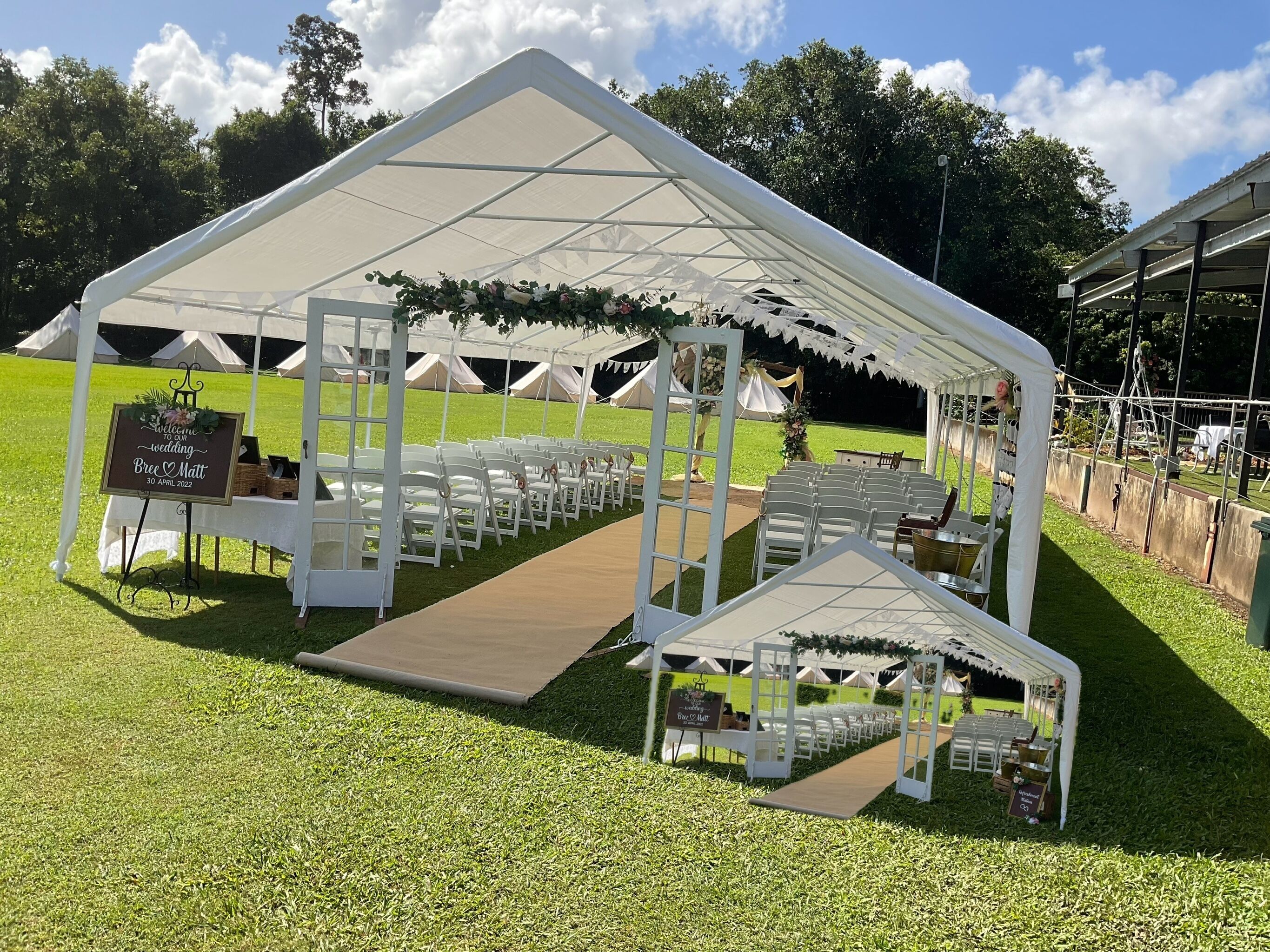 A tented wedding setup with white chairs and a wooden aisle.