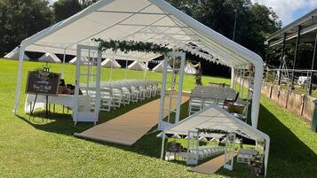 A tented wedding setup with white chairs and a wooden aisle.