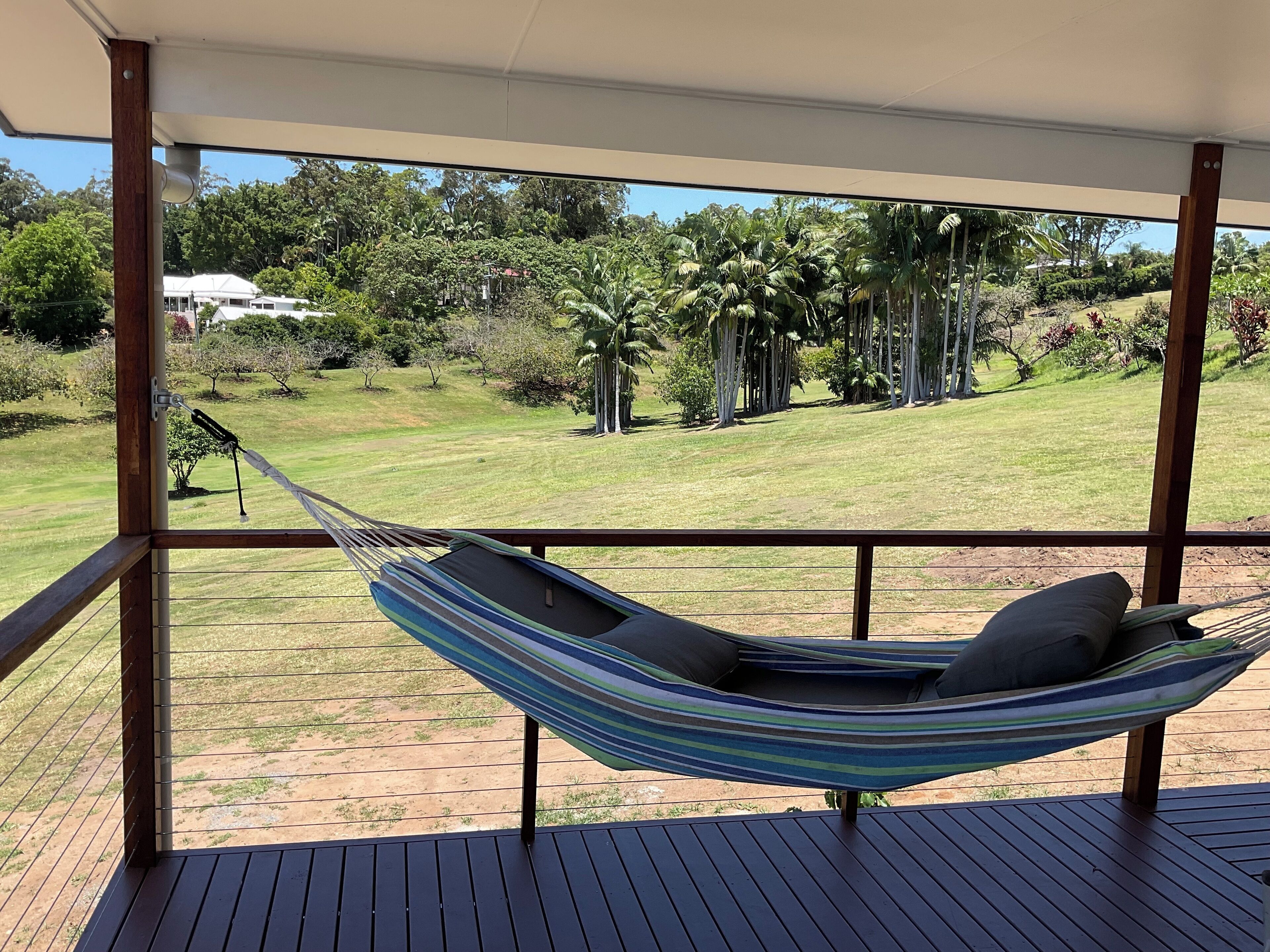 A hammock on a wooden deck with a view of a grassy area and trees.
