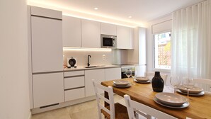 Eine moderne Küche mit weißen Schränken, einem Holztisch und Blick ins Freie durch ein Fenster.