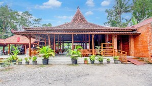 A traditional building with a tiled roof and wooden structure, surrounded by potted plants and a gravel ground. - Capital O 93873 Sokkyo Homestay (Ngaglik)